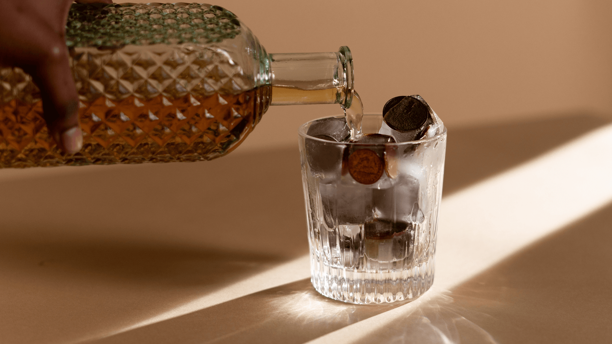 person-pouring-whiskey-into-drinking-glass-with-ice